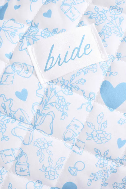 Close-up of a white quilted fabric with light blue floral and heart patterns, featuring a sewn-on label that reads 'bride'.