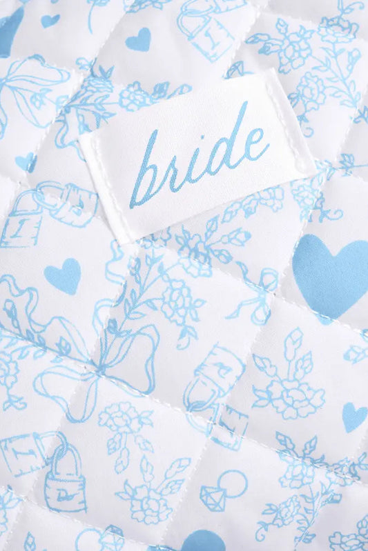 Close-up of a white quilted fabric with light blue floral and heart patterns, featuring a sewn-on label that reads 'bride'.