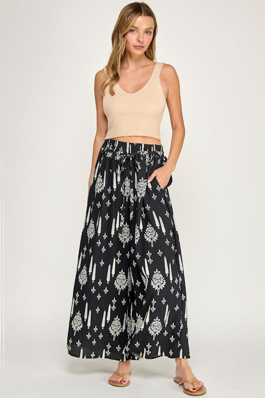 Woman wearing a beige top and black patterned pants on a white background