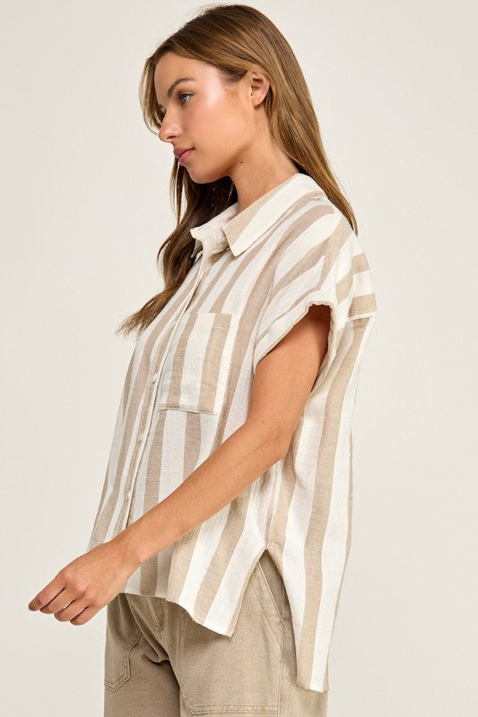 A woman wearing a beige and white vertically striped short-sleeve button-up shirt, paired with beige pants, photographed against a solid off-white studio background.