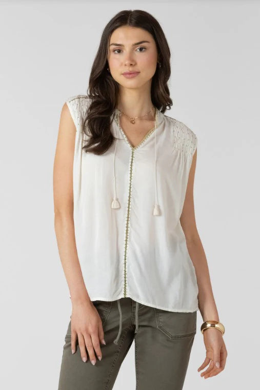 Woman wearing a white sleeveless blouse with a zipper and green pants on a white background