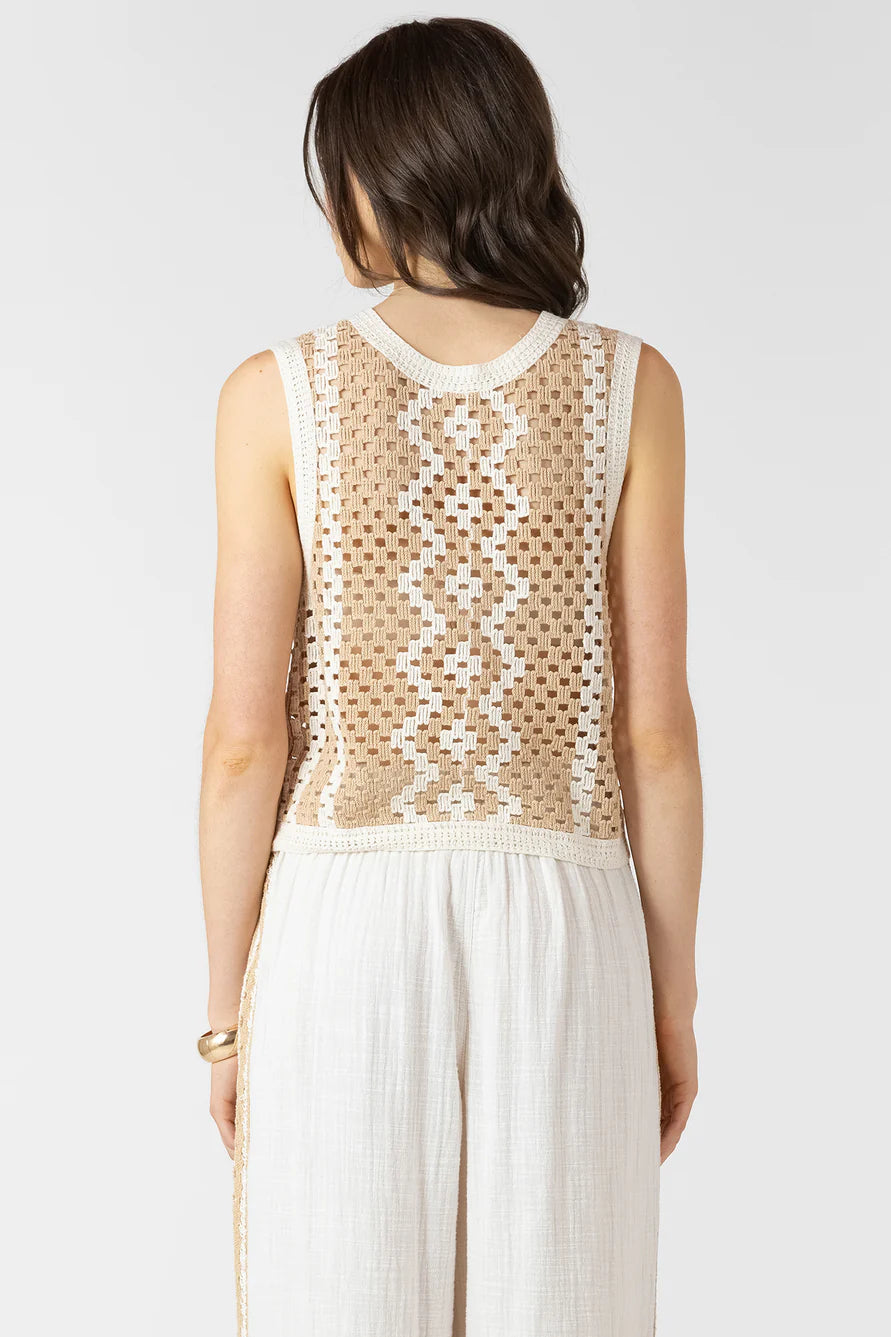 Woman wearing a sleeveless beige and white patterned top with a plain white skirt on a light gray background