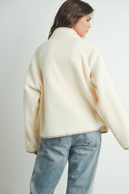 A woman shown from the back wearing a cream-colored, textured knit sweater and light blue jeans against a plain light gray background.