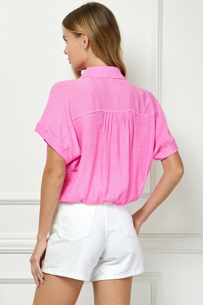 Woman wearing a pink shirt and white shorts against a white wall