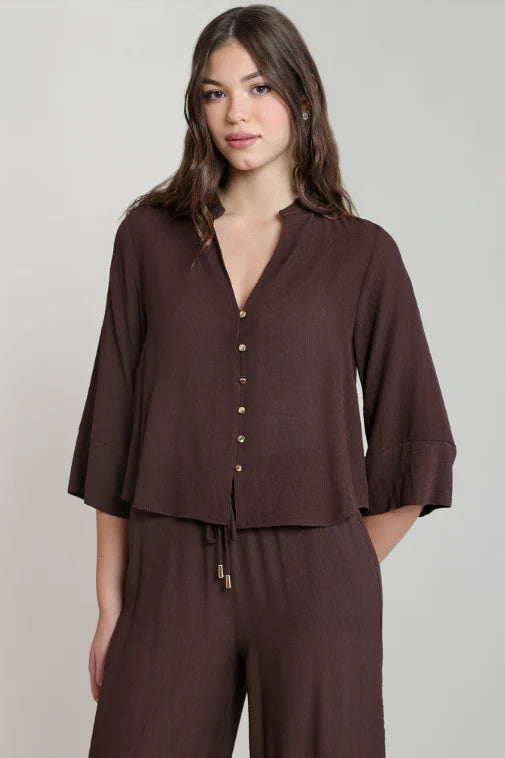 A woman modeling a dark brown button-front top with three-quarter sleeves and matching wide-leg pants against a plain light gray studio background.