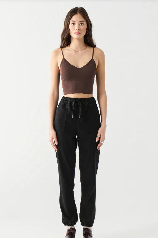 A woman modeling a dark brown spaghetti-strap crop top and black drawstring sweatpants against a plain light gray studio background.