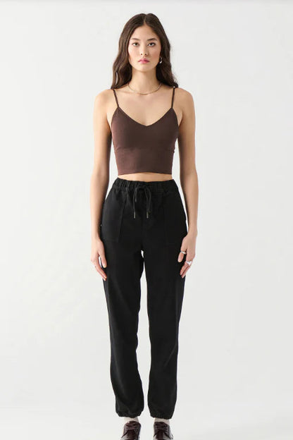 A woman modeling a dark brown spaghetti-strap crop top and black drawstring sweatpants against a plain light gray studio background.