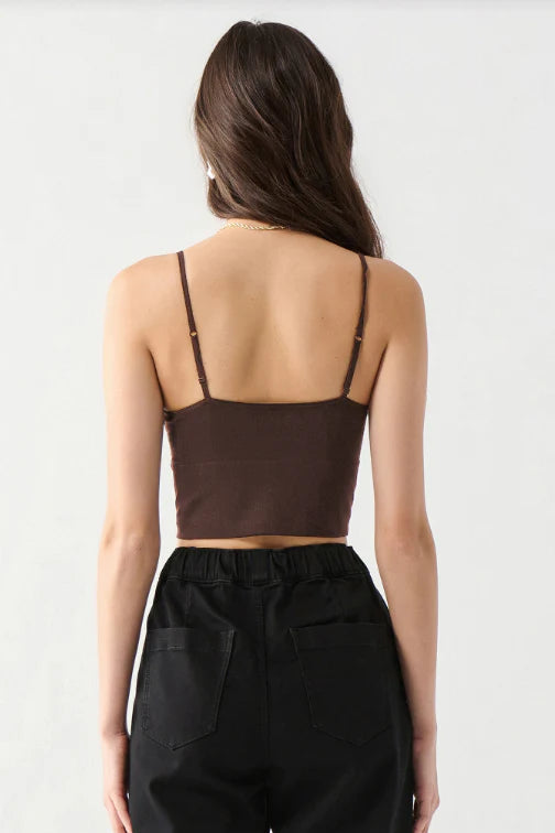A woman shown from the back wearing a dark brown spaghetti-strap crop top and black pants, photographed against a plain light gray studio background.