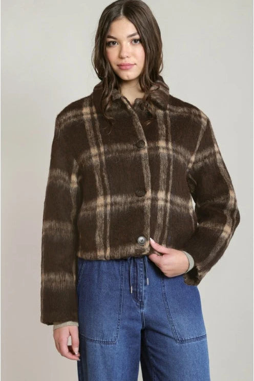 A woman wearing a cropped brown plaid faux fur jacket with a high collar and button front, paired with blue jeans, against a neutral light gray background.