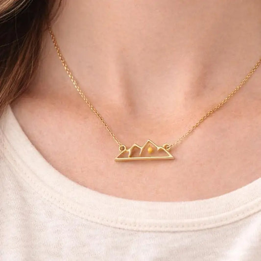 Gold necklace with mountain design on a person wearing a white shirt