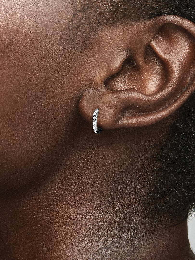 Close-up of an ear wearing a diamond hoop earring on a neutral background