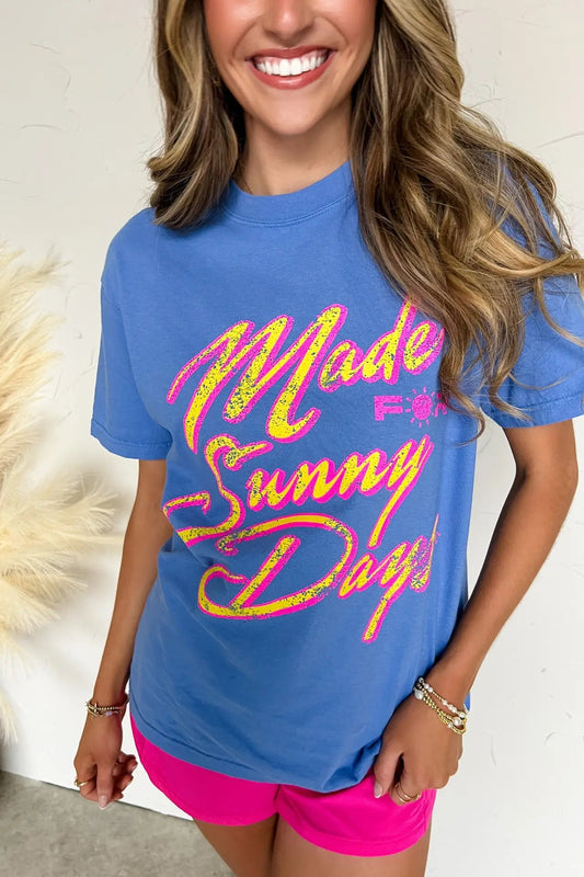 Woman wearing a blue t-shirt with colorful text, standing against a neutral background.