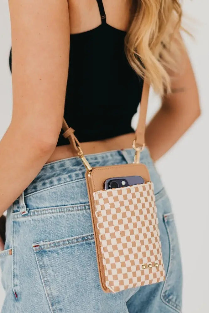 Person holding a phone case with a checkered pattern and brown strap.