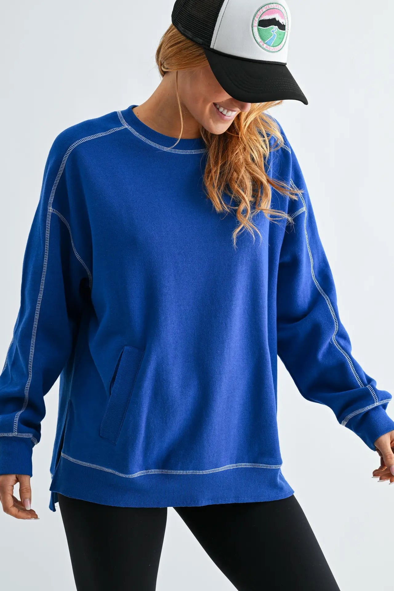 Person wearing a blue sweatshirt and black cap with a white visor on a light gray background