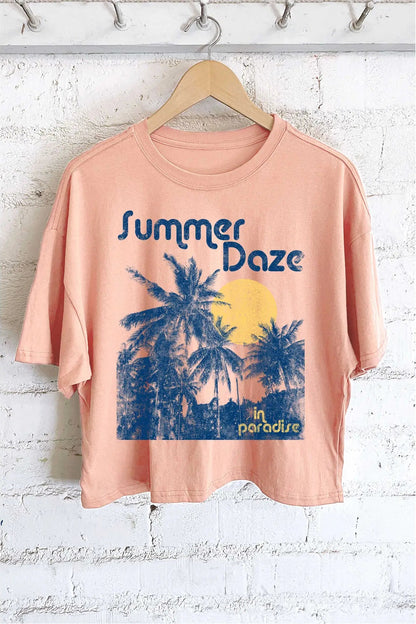 Peach t-shirt with 'Summer Daze in Paradise' graphic on a hanger against a white brick wall.