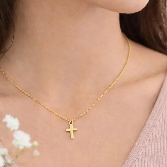 Gold necklace with a cross pendant worn by a person, with a blurred background.