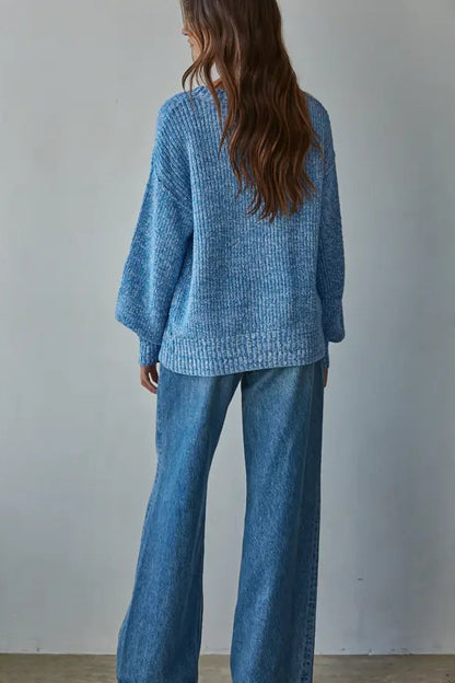 Person wearing a blue knitted sweater and jeans against a plain background