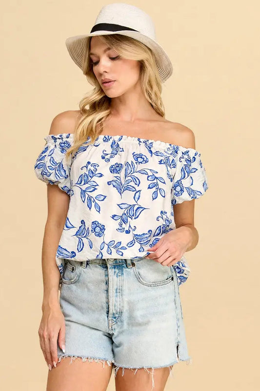 Woman wearing a floral off-shoulder top and denim shorts on a beige background