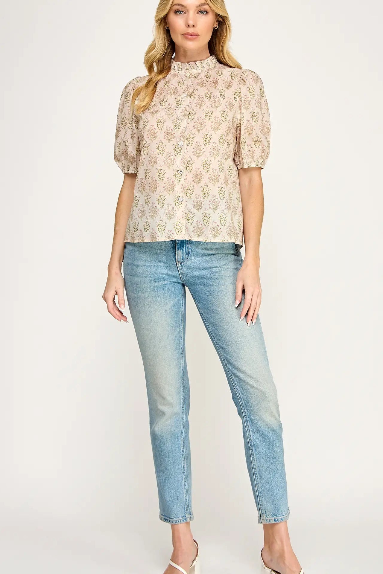 Woman wearing a patterned blouse and light blue jeans on a white background