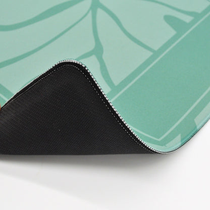 A close-up of a gaming mouse pad showing its black textured underside and a mint green top surface with a subtle leaf pattern, folded over on a white surface.