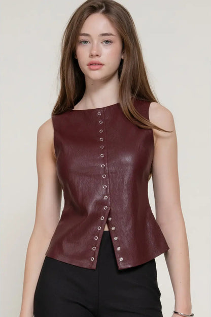 A woman modeling a sleeveless, structured burgundy faux-leather top with a front button closure, paired with black pants, against a plain light beige background.