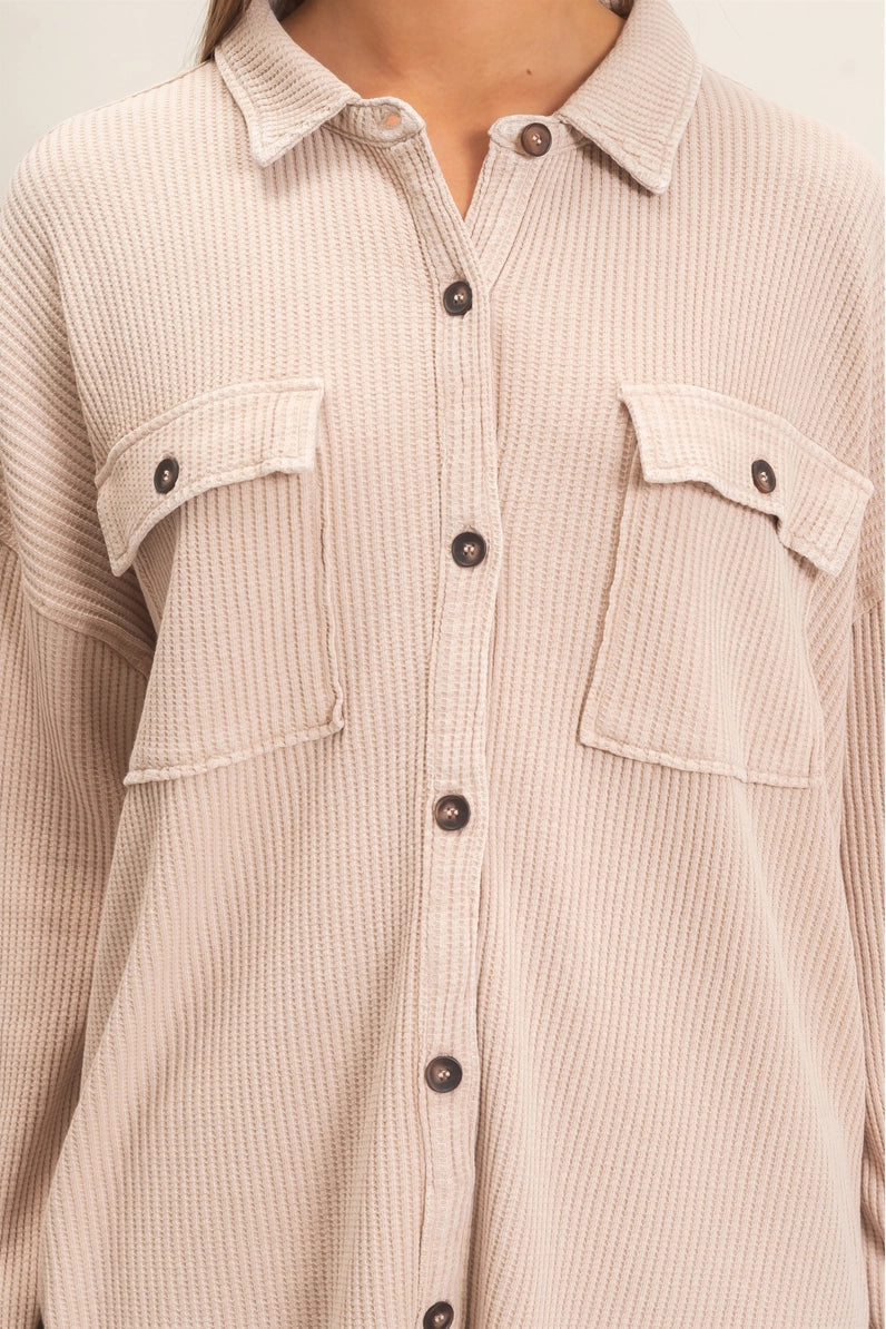 A close-up of a person wearing a light beige ribbed button-up shirt with two chest flap pockets and dark buttons, shown against a plain light background.