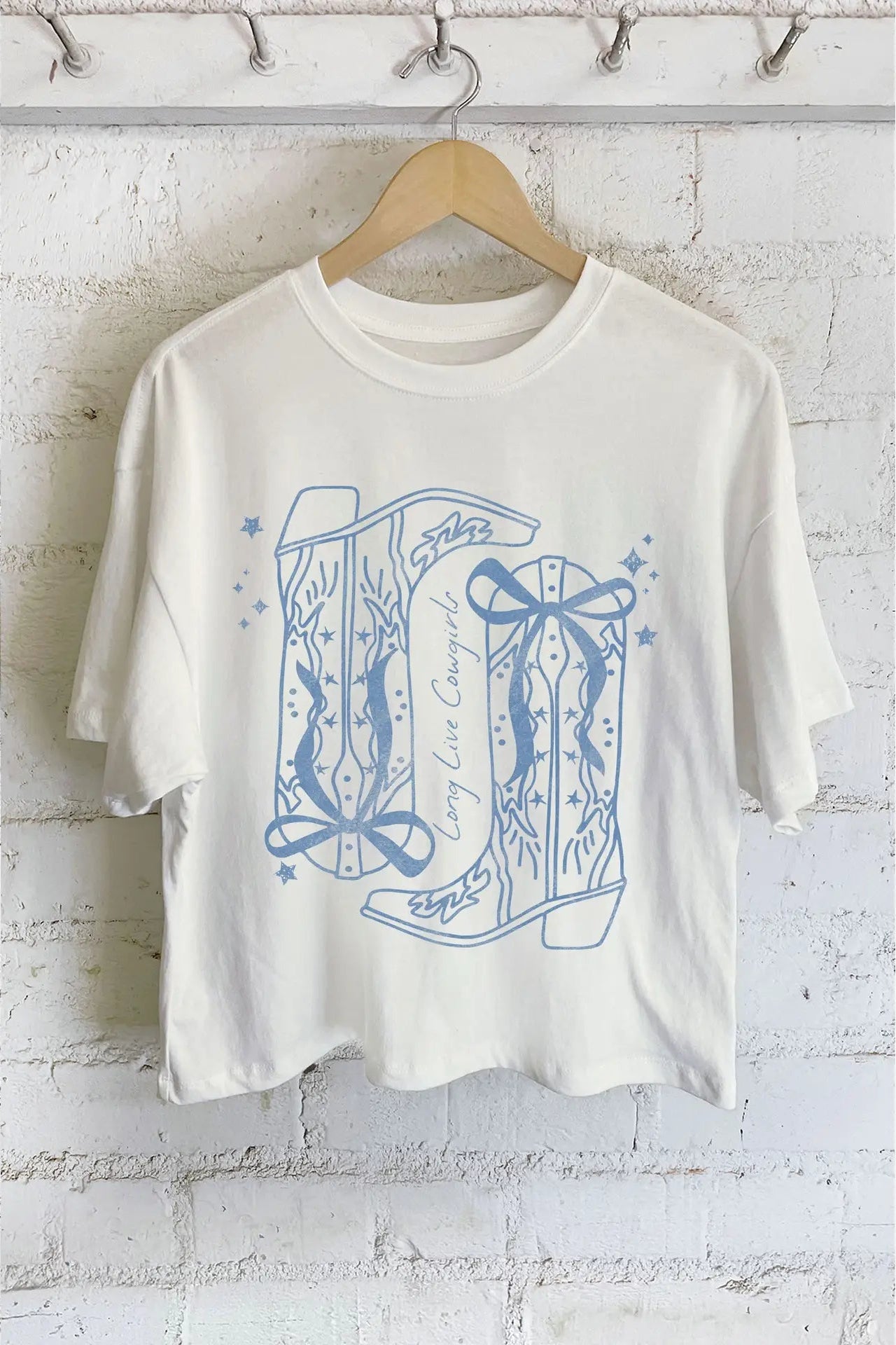 White t-shirt with blue graphic design on a wooden hanger against a white brick wall.