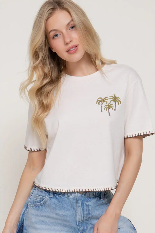 Woman wearing a white t-shirt with palm tree design on a plain background