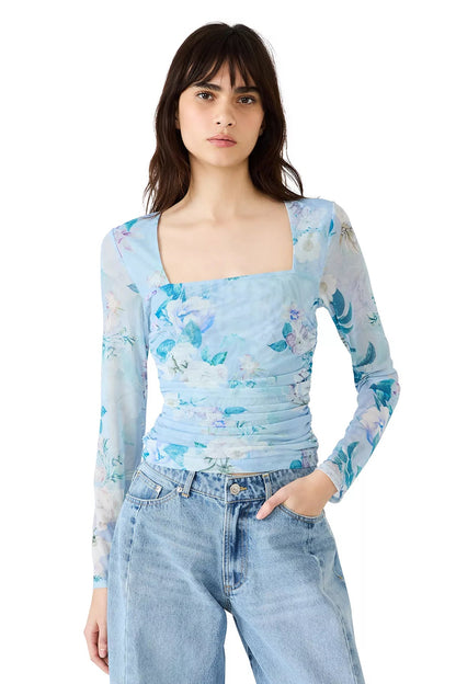 Woman wearing a light blue floral long-sleeve top and jeans on a white background