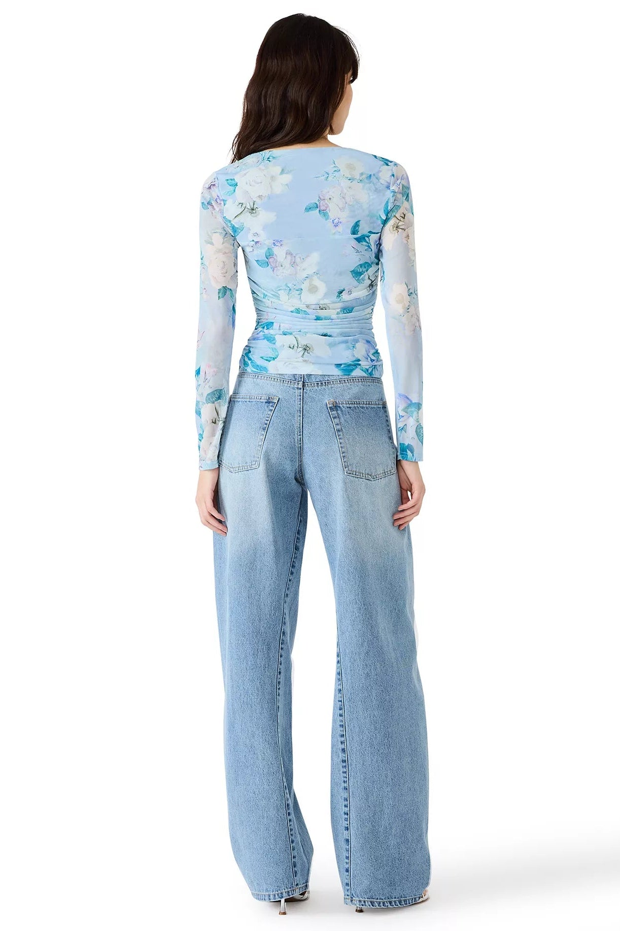 Woman wearing a light blue floral long-sleeve top and jeans on a white background
