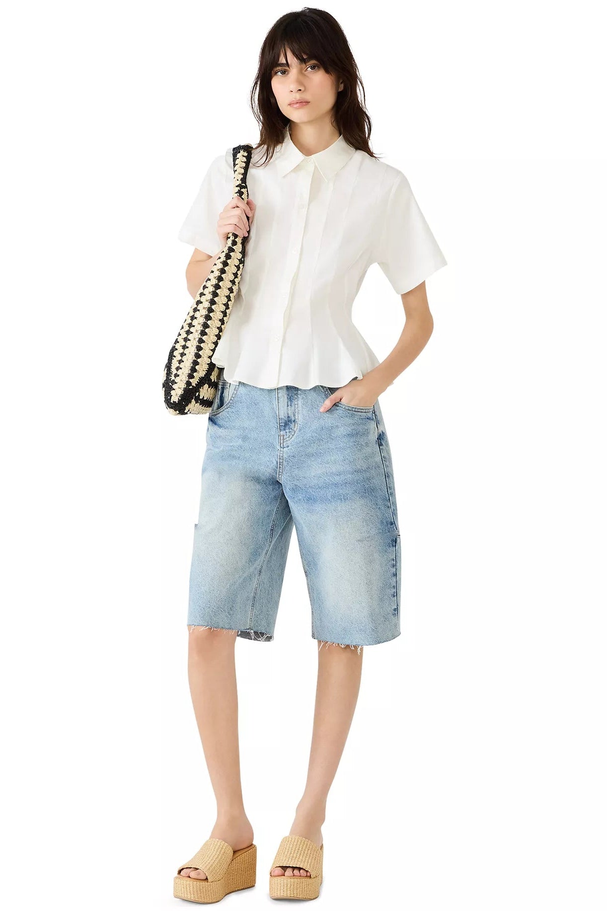 Woman wearing a white shirt and light blue denim shorts holding a black and white bag on a white background