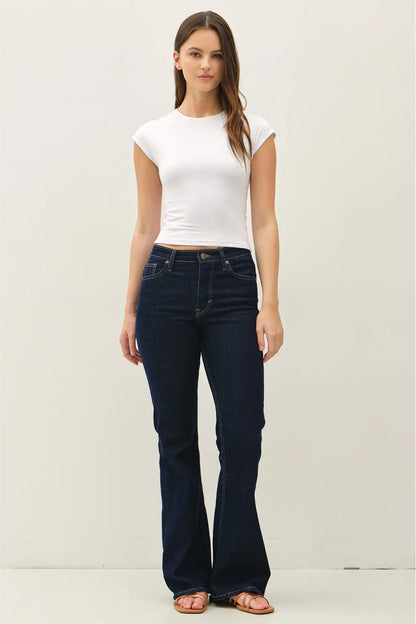 Woman wearing a white t-shirt and dark blue jeans against a plain background