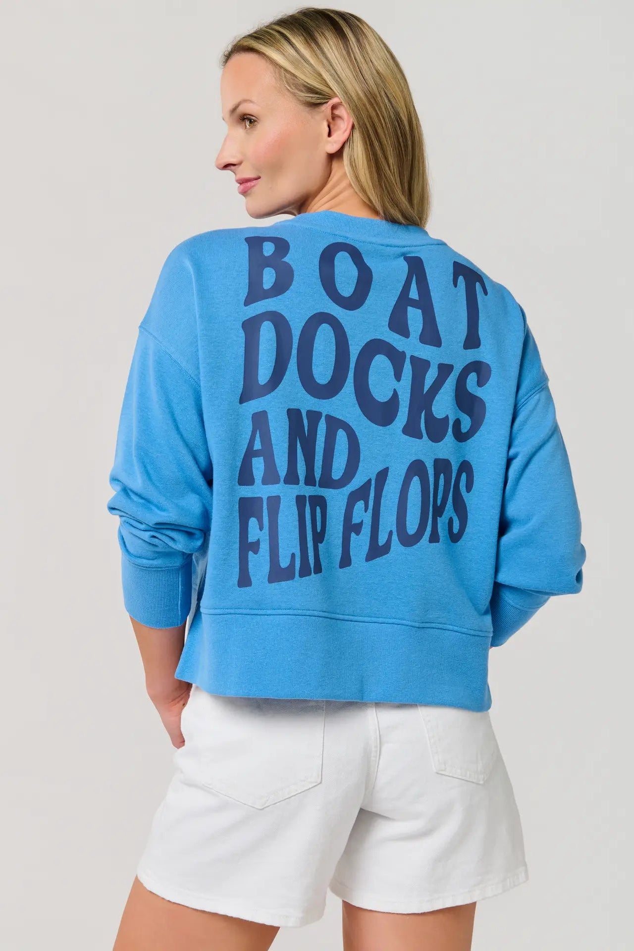 Person wearing a blue sweatshirt with text on the back, standing against a plain background