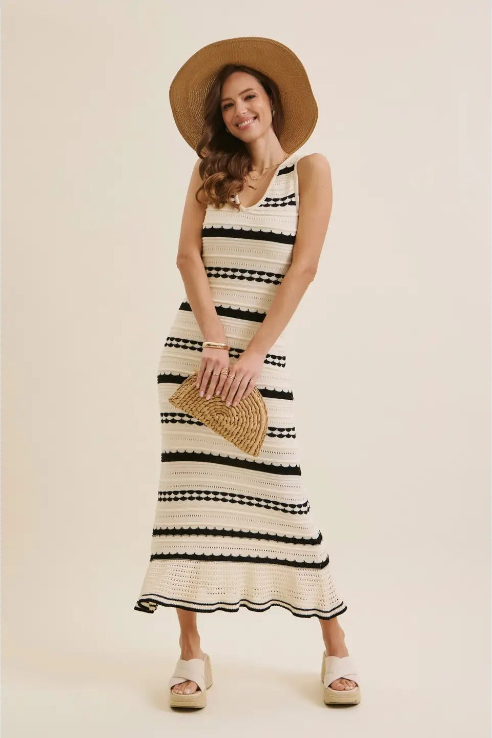 Woman wearing a black and white striped dress with a straw hat and bag on a beige background
