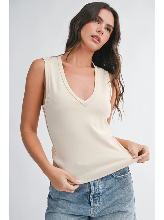 Woman wearing a beige sleeveless top and blue jeans on a white background