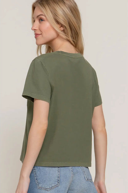 Woman wearing an olive green t-shirt and blue jeans against a plain background