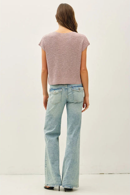 Woman wearing a pink textured top and light blue jeans on a white background