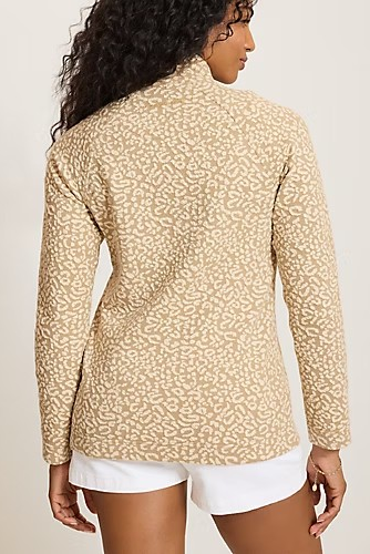 A woman shown from the back wearing a beige long-sleeve top with a fine tonal abstract pattern and white shorts against a plain light background.