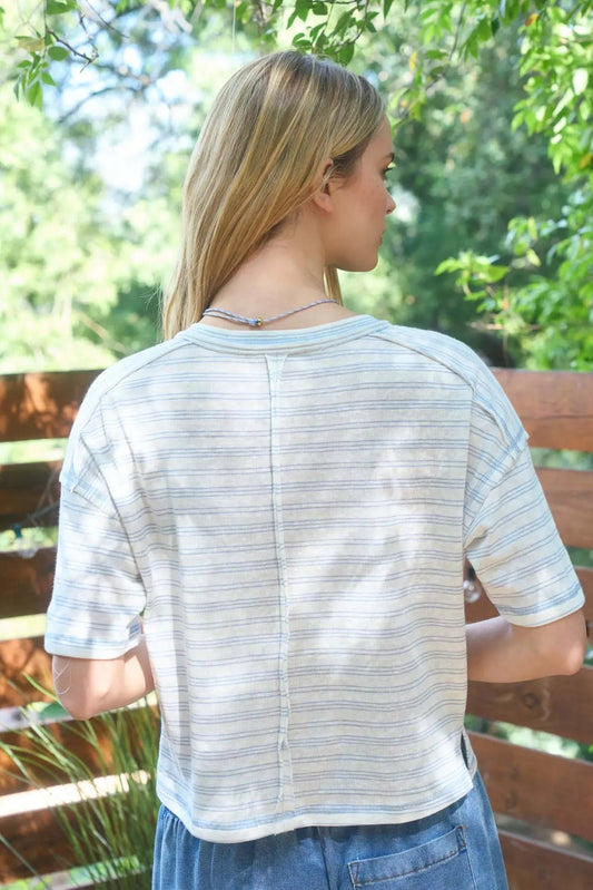 Woman wearing a striped shirt and blue jeans standing outdoors with greenery in the background