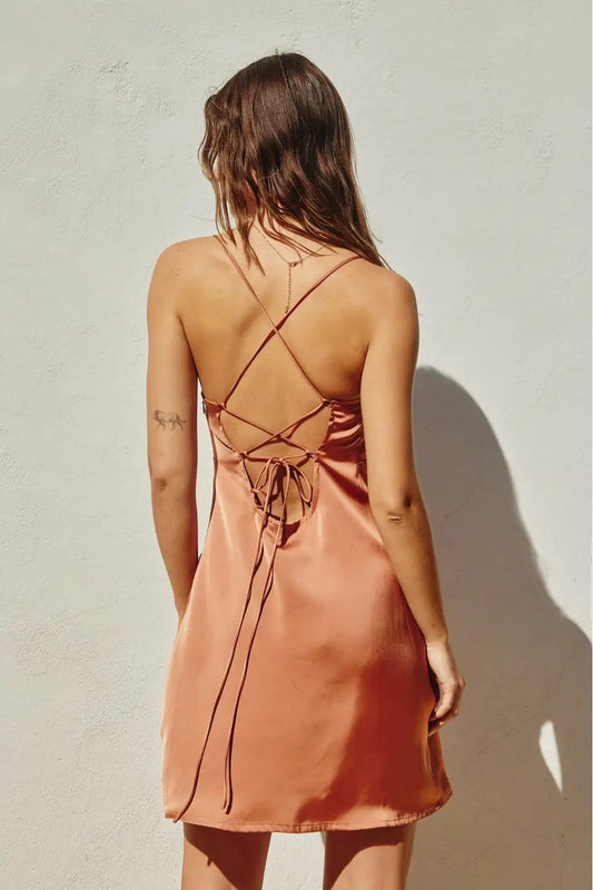 Woman wearing a pink satin dress with thin straps against a light background