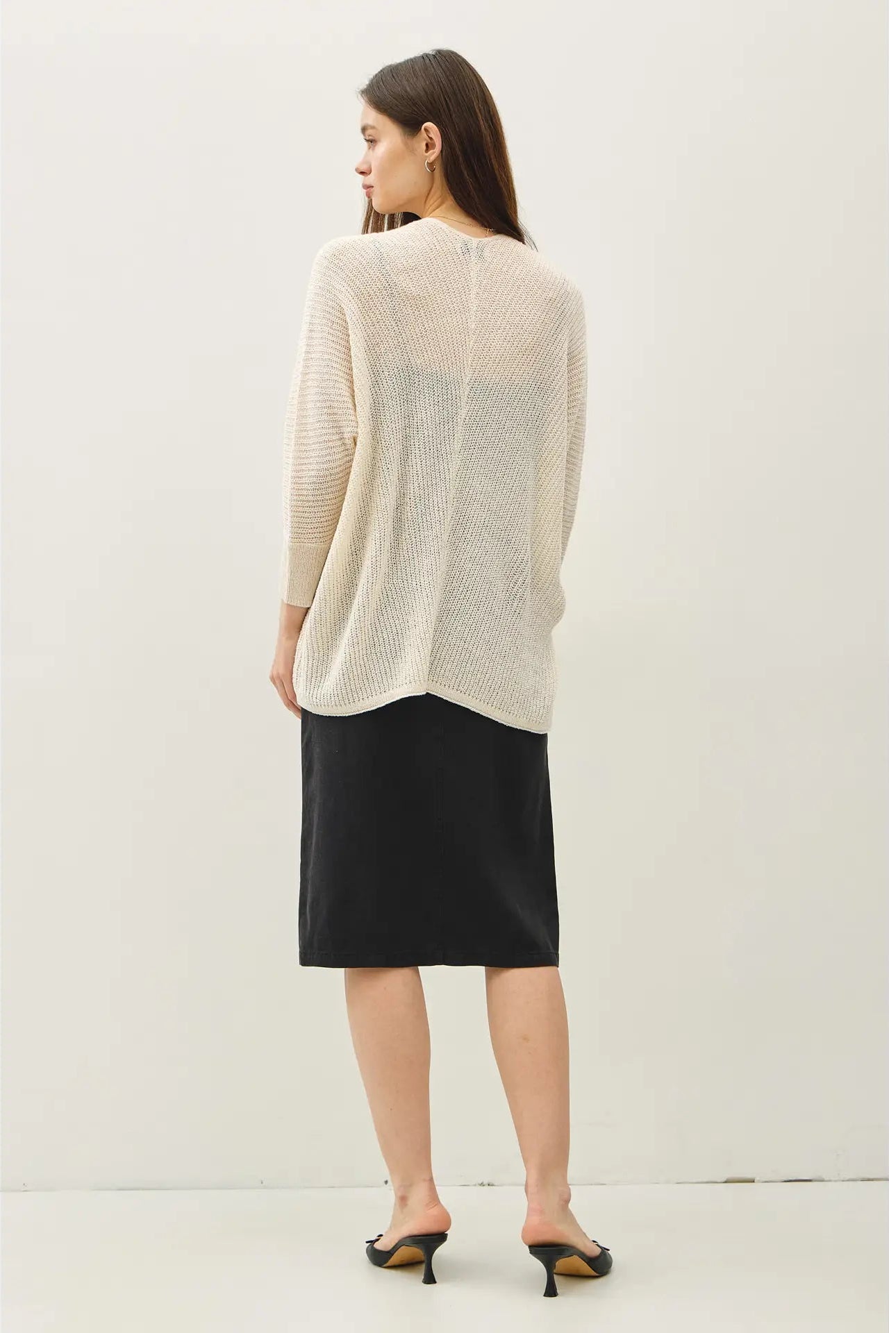 Woman wearing a cream sweater and black skirt on a white background