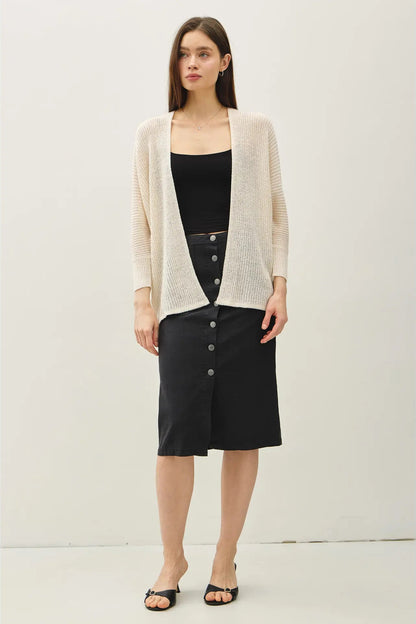Woman wearing a beige cardigan over a black top and skirt on a white background