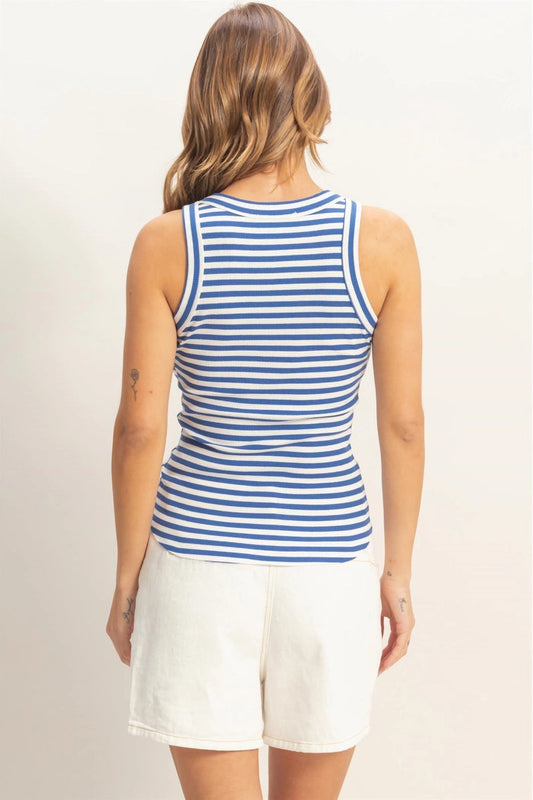 Woman wearing a blue and white striped tank top and white shorts on a plain background