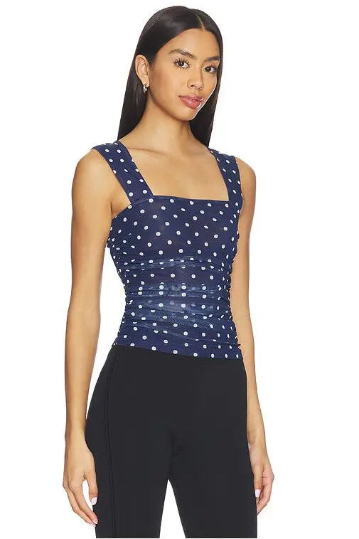 Woman wearing a navy blue sleeveless top with white polka dots on a white background