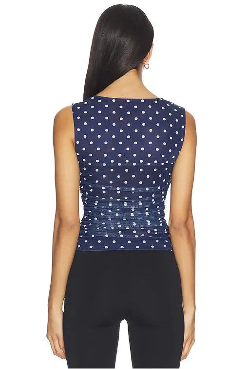 Woman wearing a navy blue sleeveless top with white polka dots on a white background