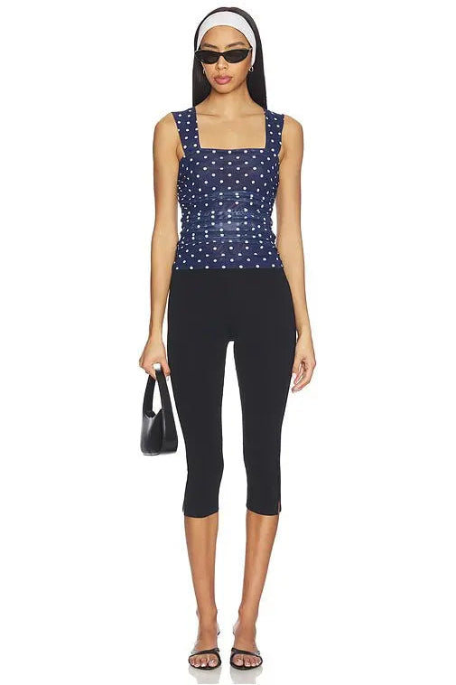 Woman wearing a navy blue sleeveless top with white polka dots and black capri pants on a white background.