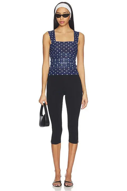Woman wearing a navy blue sleeveless top with white polka dots and black capri pants on a white background.