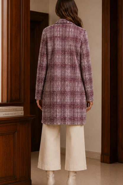 A woman viewed from behind wearing a long-sleeve plaid coat in dusty purple and white, paired with cream wide-leg trousers and white boots, standing in a room with dark wood paneling.