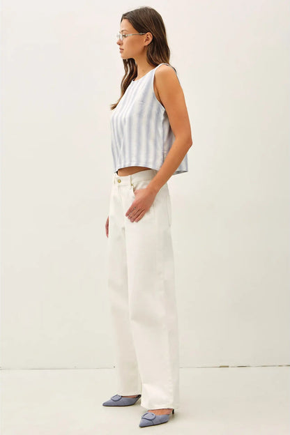 Woman wearing a striped sleeveless top and white pants against a plain background