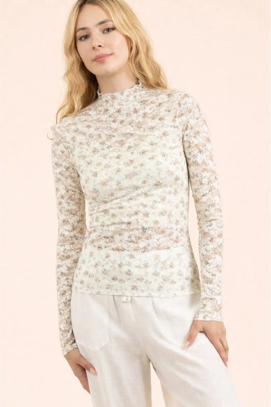 Woman wearing a floral long-sleeve top and white pants against a light pink background